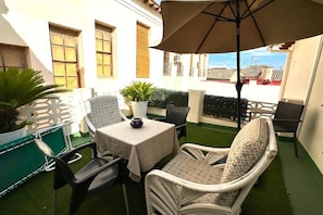 Een terras buiten met een tafel, stoelen en een parasol.