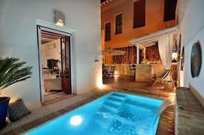 A pool area with a hot tub, outdoor seating, and a view of the interior.
