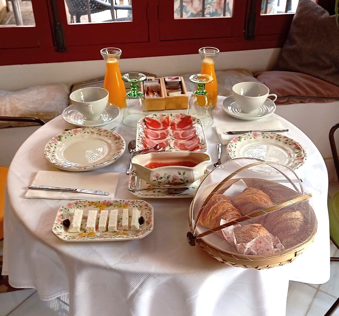 A breakfast setup with plates, cups, a basket of bread, and juice bottles on a table.