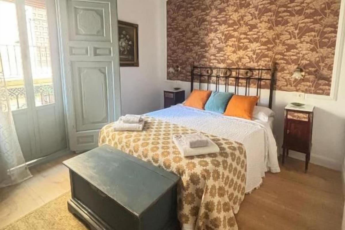 Een slaapkamer met een bed, nachtkastje, kaptafel en een behang met patroon.