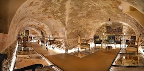An underground dining area with stone arches, tables, chairs, and a bar counter.