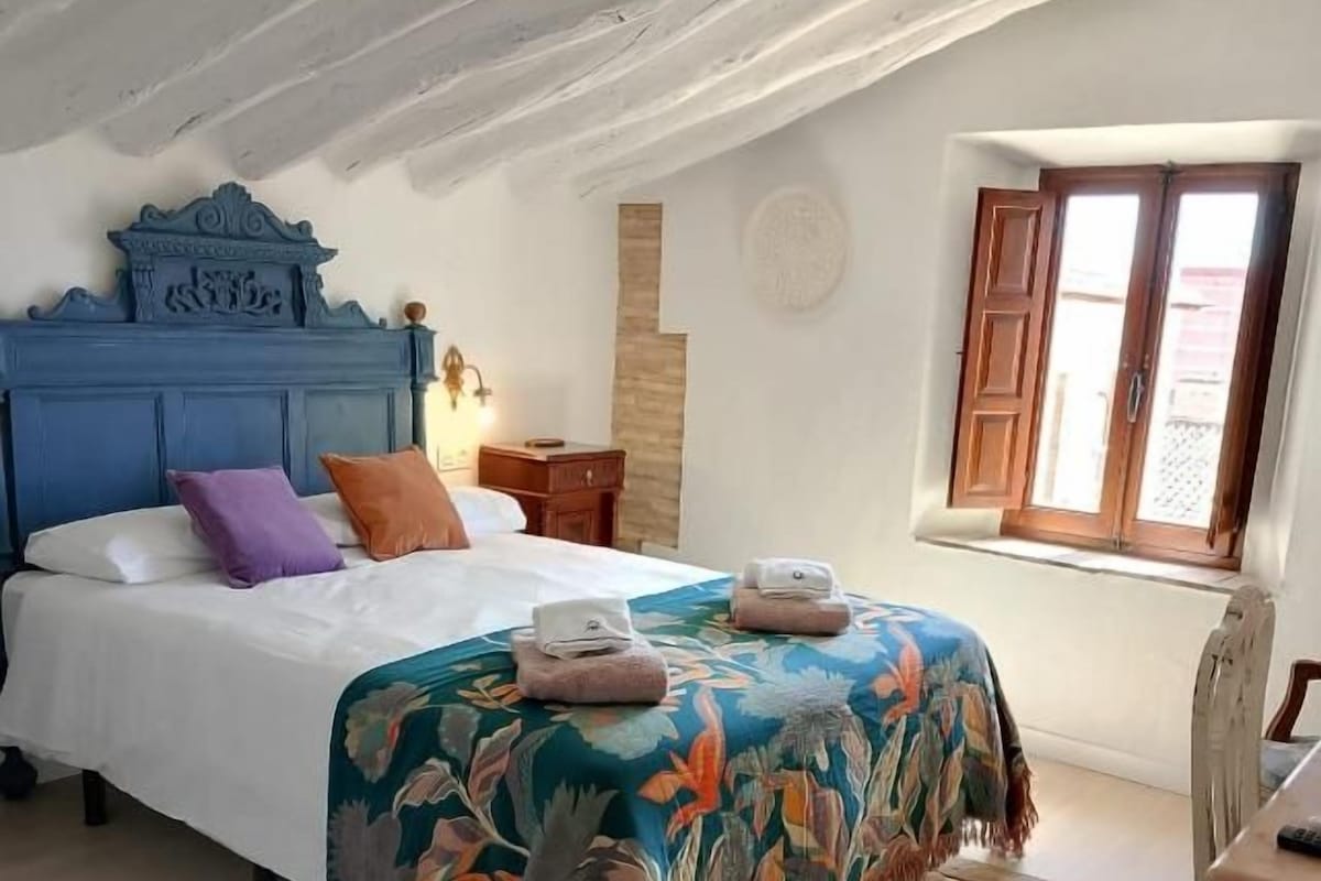 Een slaapkamer met een bed, een houten hoofdbord, een raam en een klein tafeltje.