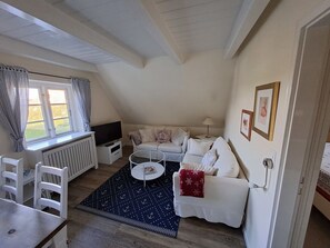 A cozy living room with a sofa, a small coffee table, a TV, and a window with curtains. - Deichhof Apt. 21 (Dunsum)