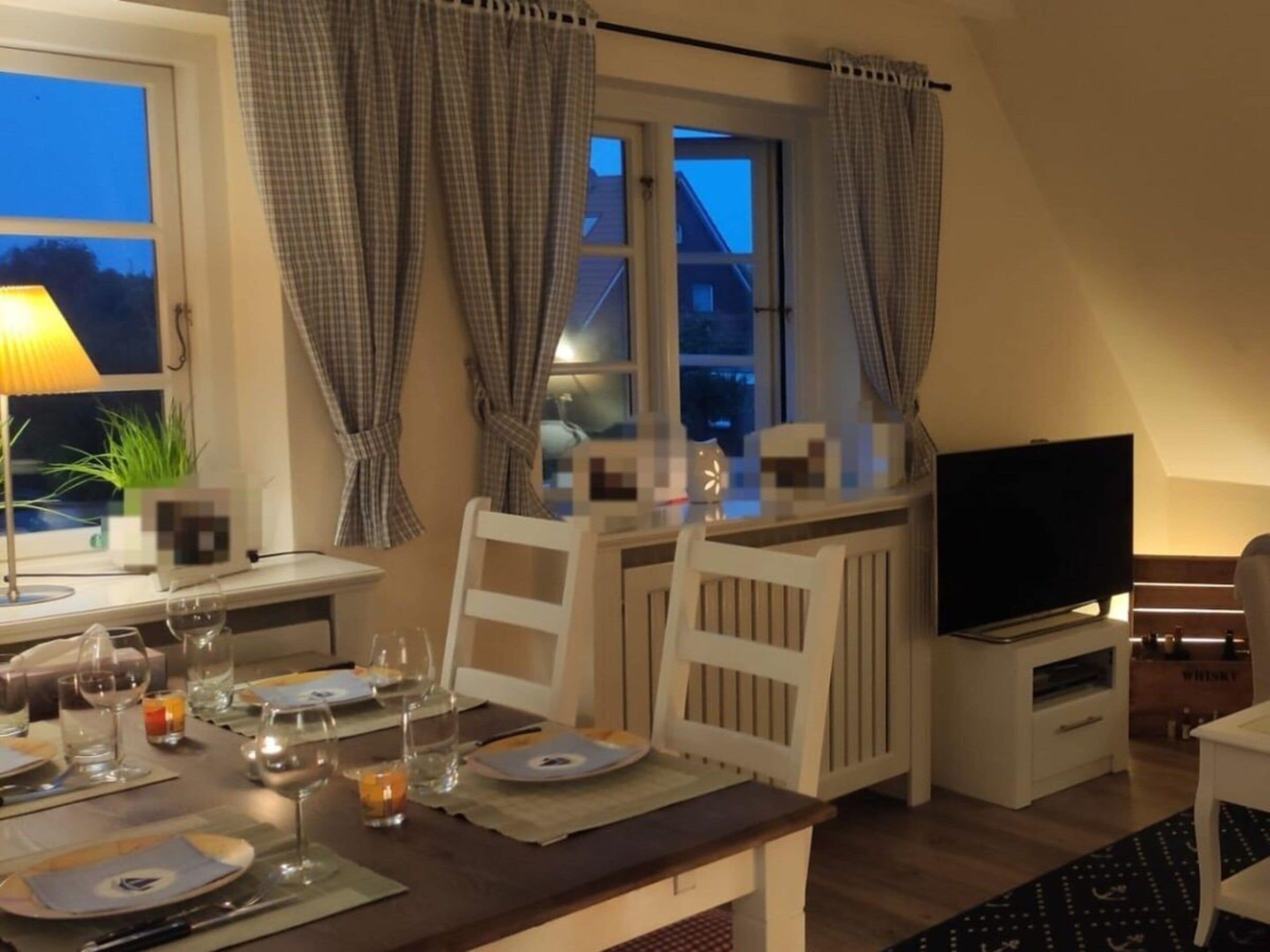 A dining area with a table set for two, a television, and a window with curtains.