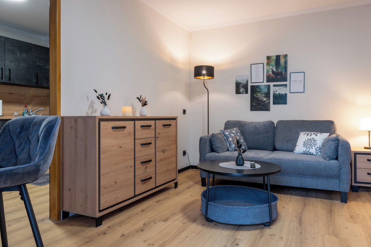 Ein modernes Wohnzimmer mit einem grauen Sofa, einer Holzeinrichtung, einem blauen Sessel, einem runden Couchtisch und einer Stehlampe.