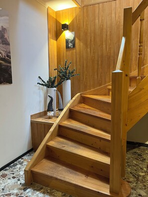 Una scala in legno con corrimano, un lampadario a parete e un quadro incorniciato.