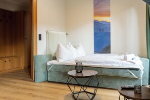 Ein Hotelzimmer mit Bett, einem kleinen Tisch, einem Sessel, einer Heizung und einem Bild von einer Berglandschaft.