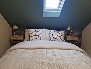 Un dormitorio con una cama, dos mesitas de noche, un tragaluz y un cabecero.