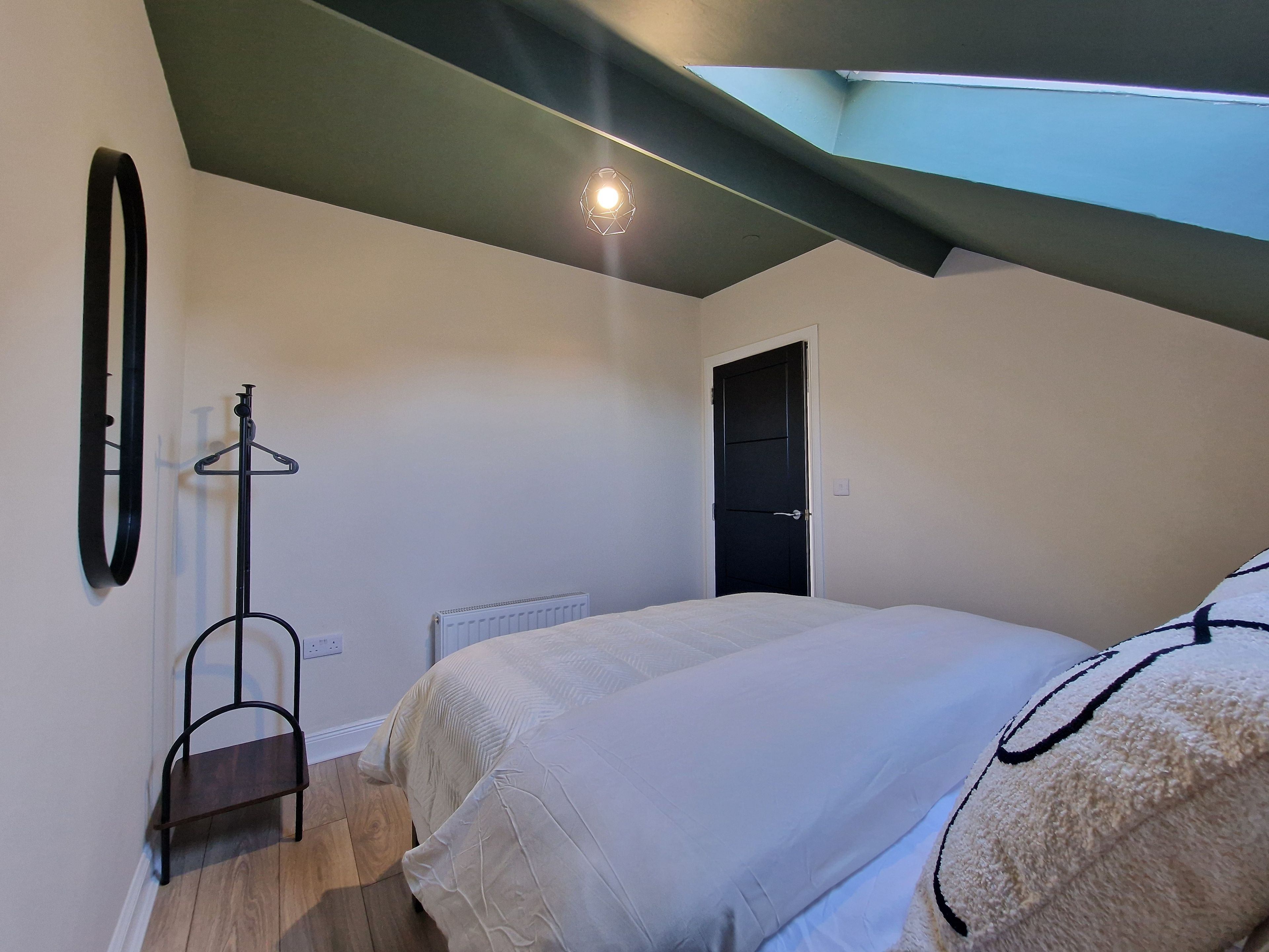 A bedroom with a skylight, a radiator, a coat rack, and a bed.