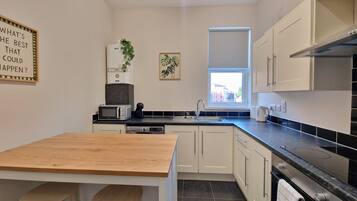 A compact kitchen with a wooden table, two stools, a microwave, a coffee maker, and a window with a view.
