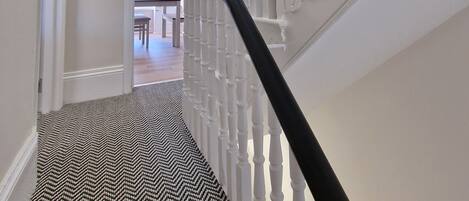 A staircase with white balusters and a black handrail leading to an open door.