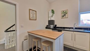 A compact kitchen with a wooden island, two stools, a microwave, a coffee maker, and a sink.