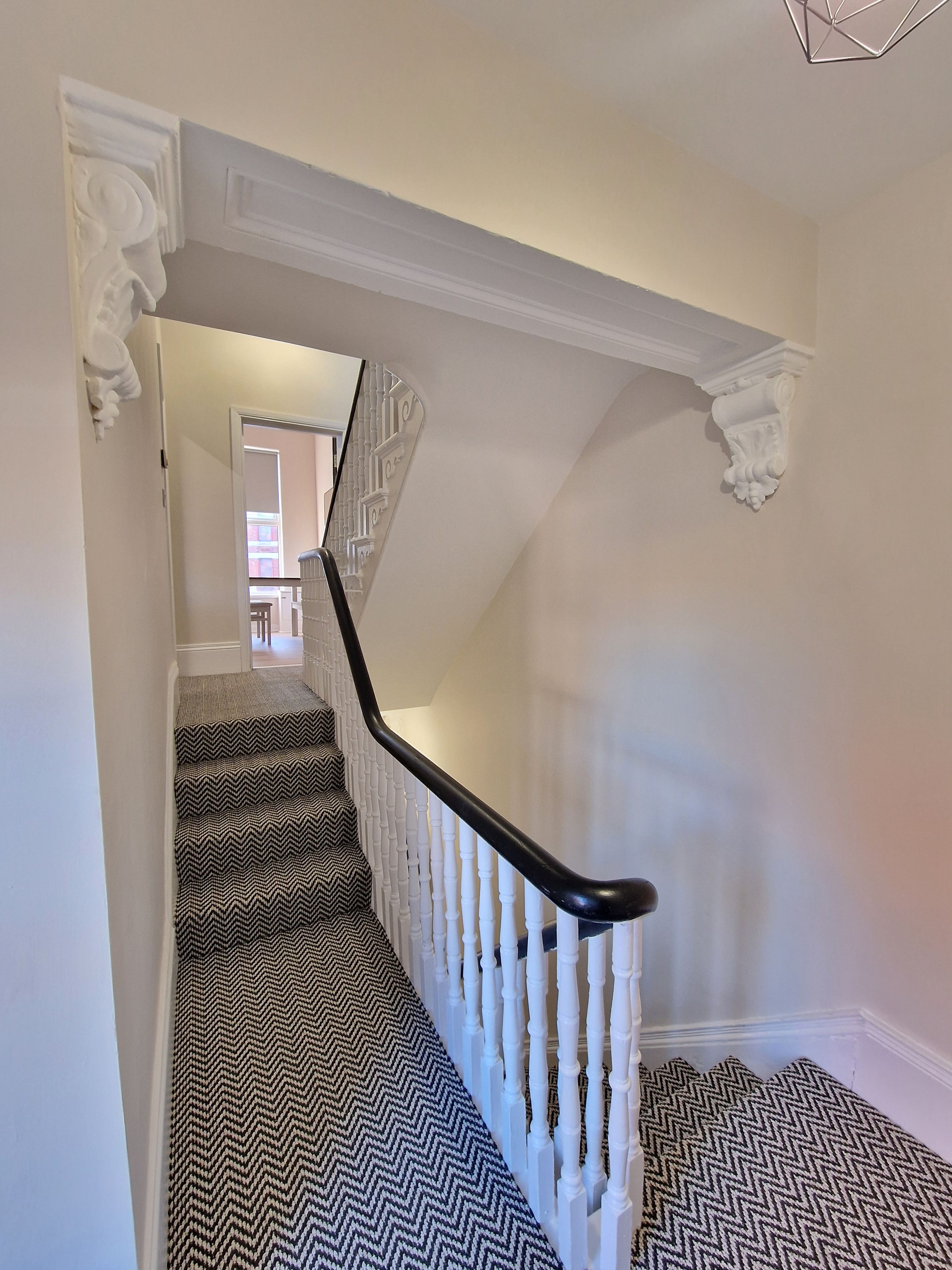 A staircase with a black and white patterned carpet, white balusters, and a black handrail.