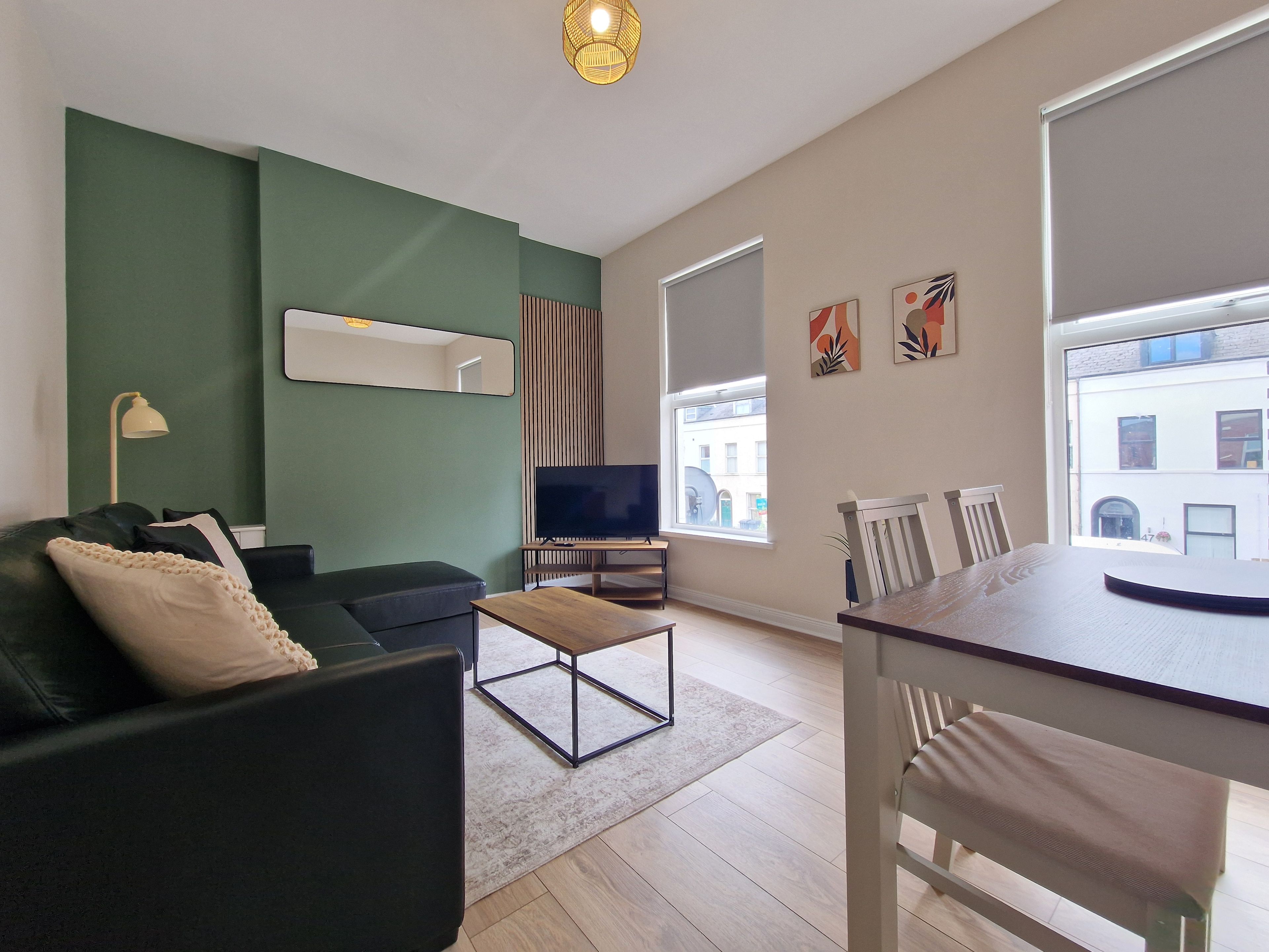 A modern living room with a sofa, a TV, a dining table, and a large window.