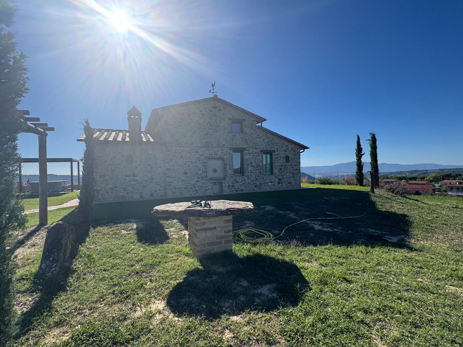 Una casa in pietra con tetto spiovente, un piccolo giardino e una vista aperta sul paesaggio circostante.