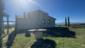 Una casa in pietra con tetto spiovente, un piccolo giardino e una vista aperta sul paesaggio circostante.
