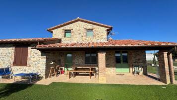 Un edificio in pietra con un patio, posti a sedere all'aperto e un prato.