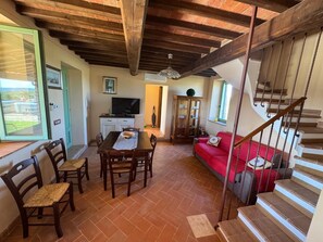 Zona pranzo con tavolo e sedie, televisione, mobile contenitore e divano rosso.