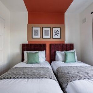 A hotel room with two beds, each with a patterned bedspread and pillows. - Newcastle - House - Sleeps 7 - Transport Links (Newcastle-upon-Tyne)