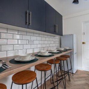 A kitchen with white subway tiles, dark cabinets, and a wooden countertop with stools. - Newcastle - House - Sleeps 7 - Transport Links (Newcastle-upon-Tyne)