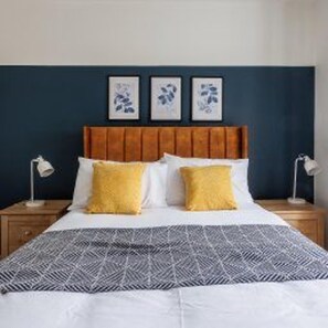 A bed with a patterned bedspread, two pillows, a wooden headboard, and bedside lamps. - Newcastle - House - Sleeps 7 - Transport Links (Newcastle-upon-Tyne)