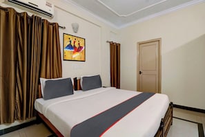 Habitació d'hotel amb un llit, cortines, un quadre i una porta.