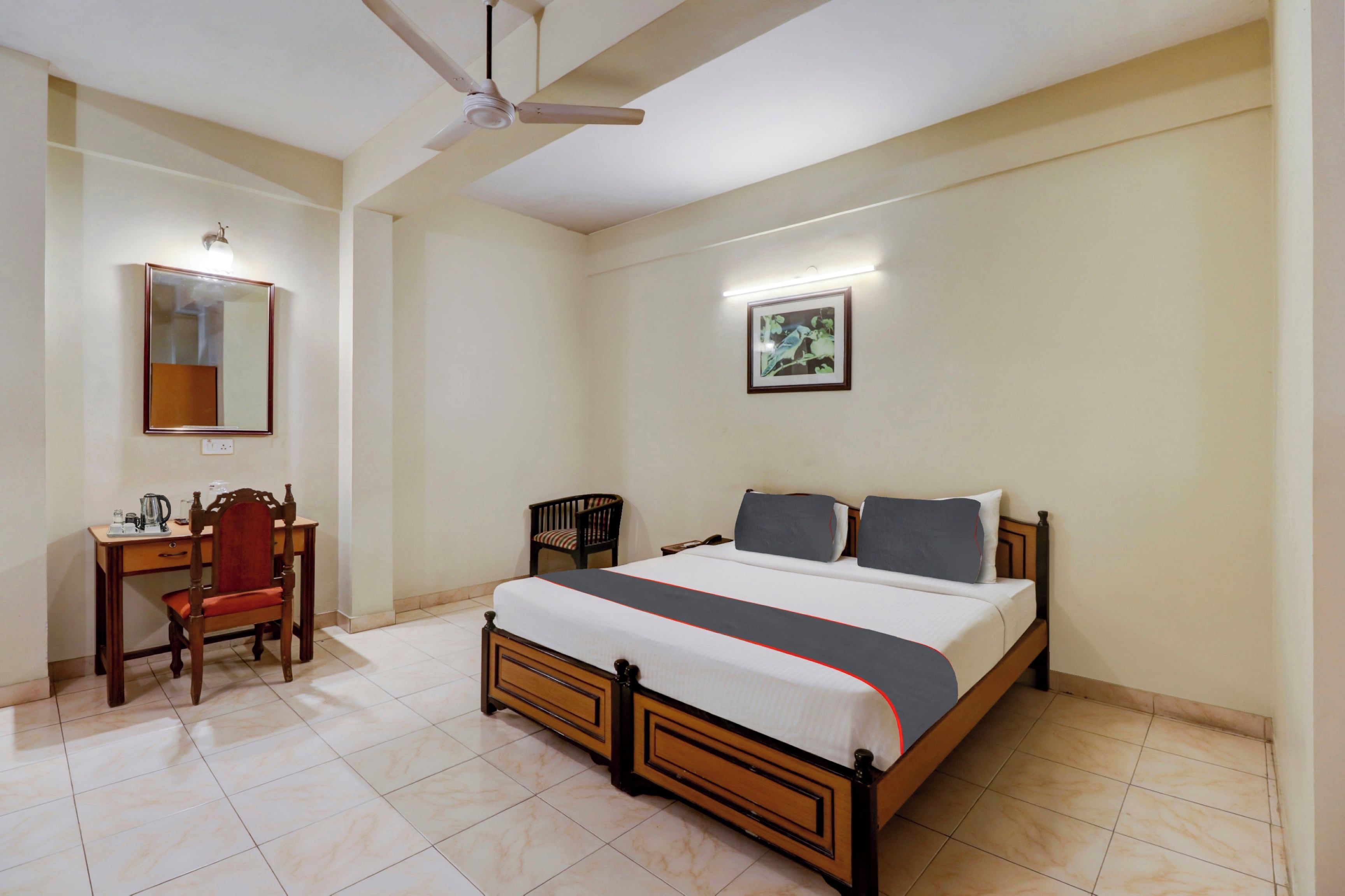 Habitación de hotel con cama, escritorio, silla, ventilador de techo y un cuadro enmarcado en la pared.