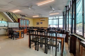 Un comedor con varias mesas y sillas, una escalera y ventanas grandes.