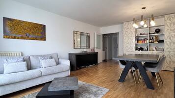 A modern living room with a grey sofa, a coffee table, and a dining area with a table and chairs.
