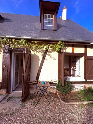 A house with a wooden balcony, a table with chairs, and a window. - Normandy farmhouse with a fireplace and a 2,800 m² enclosed garden. Pets welcome (Heudicourt)