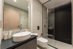 A modern bathroom with a large oval sink, a toilet, and a glass-enclosed shower area. - Stylish City Stay in Peninsula Four (Dubai)