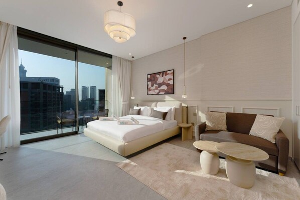 A modern hotel room with a large bed, a sofa, a coffee table, and a view of the cityscape. - Stylish City Stay in Peninsula Four (Dubai)