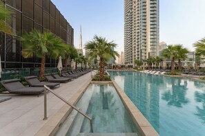 A swimming pool with lounge chairs and palm trees, surrounded by modern buildings. - Stylish City Stay in Peninsula Four (Dubai)