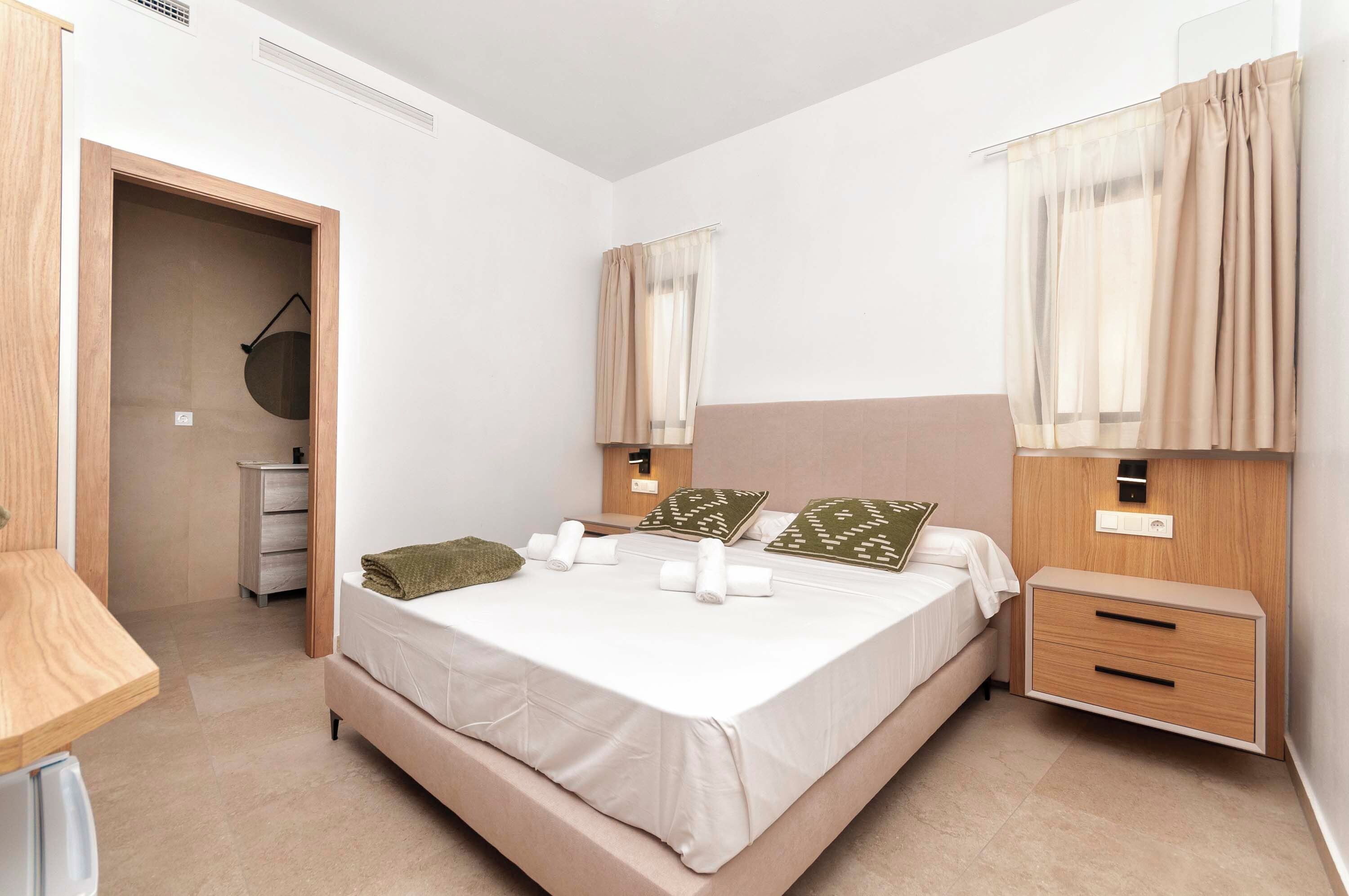 Un dormitorio con cama, mesitas de noche, un aparador de madera y un espejo circular.