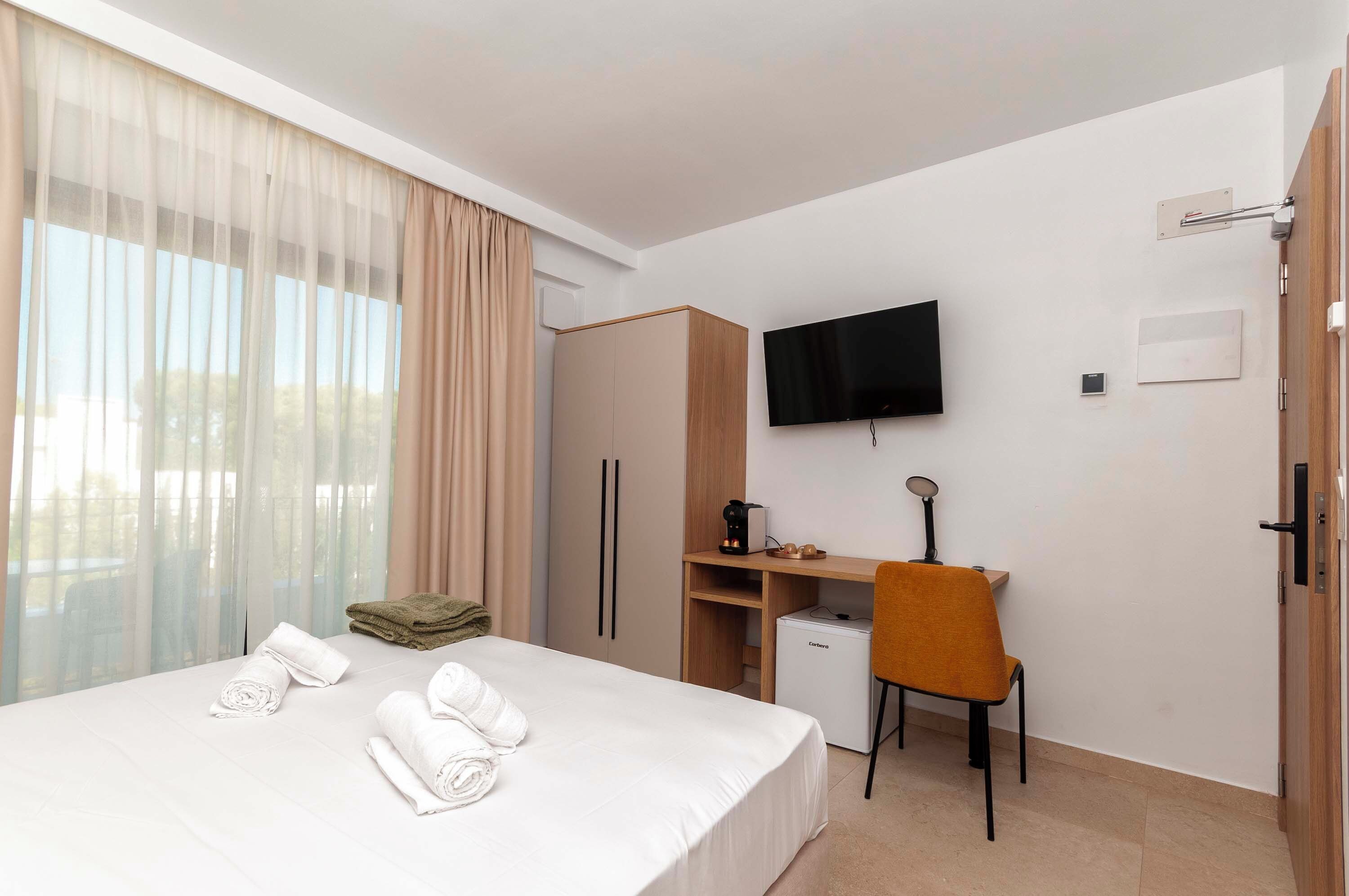 A hotel room with a bed, a desk with a chair, a television, and a wardrobe.