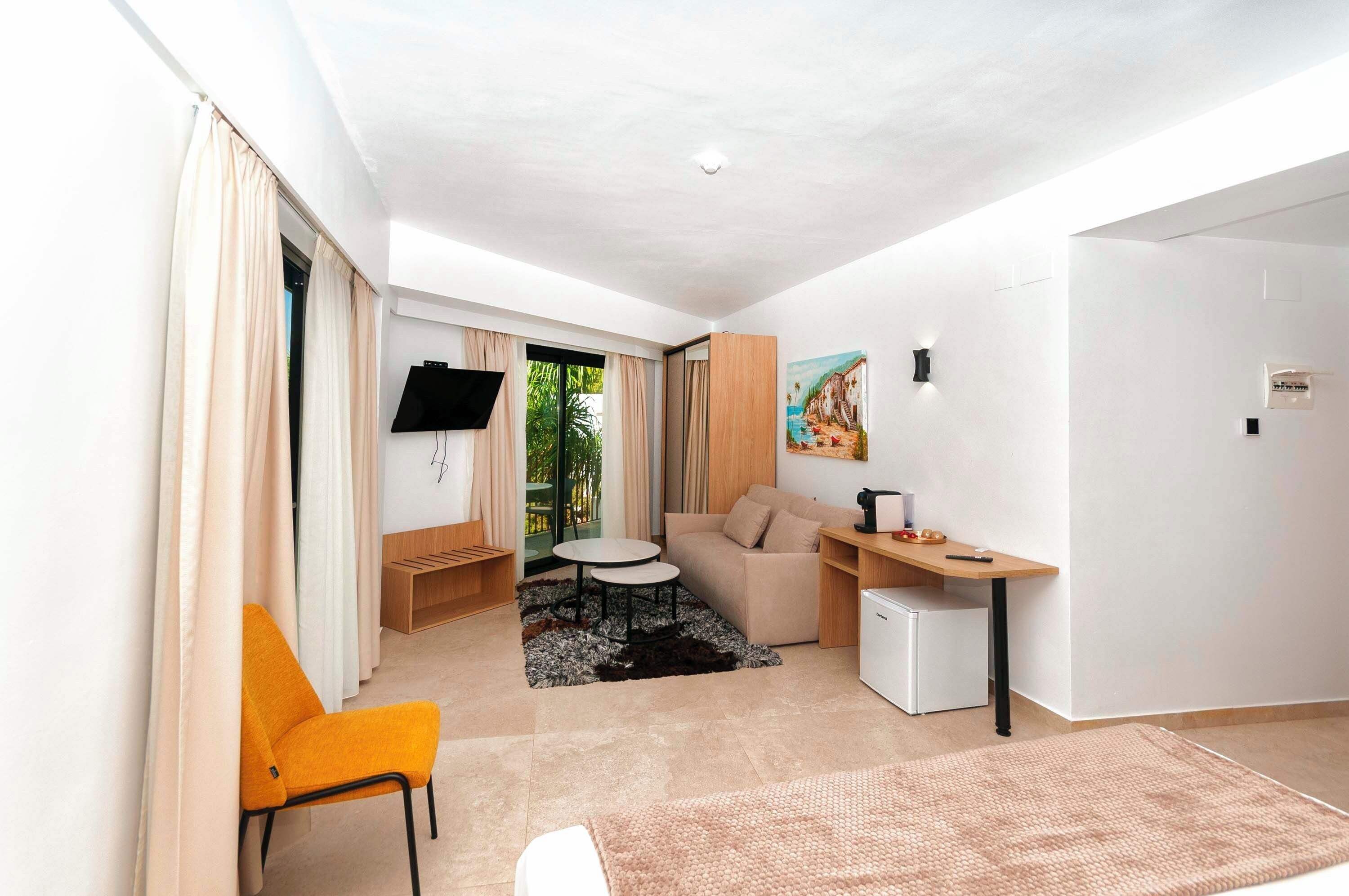 A compact hotel room with a sofa, a small table, a TV, and a painting on the wall.