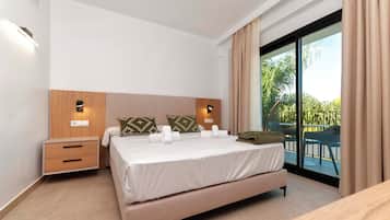 Habitación de hotel moderna con una cama grande, cabecera de madera, dos mesitas de noche y vistas al exterior a través de un ventanal corredero.
