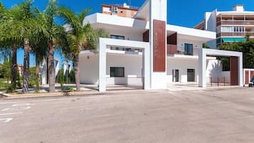 A modern hotel with a white facade, multiple balconies, and a gated entrance.
