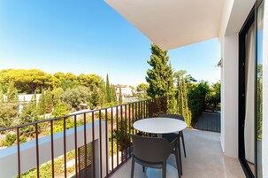 Un balcón con mesa y sillas, con vistas a un paisaje verde con árboles y edificios.