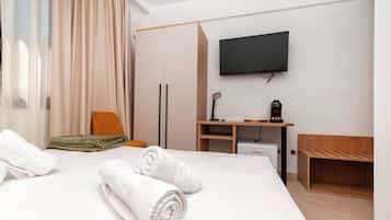 Una habitación de hotel con cama, escritorio, televisor y cafetera.