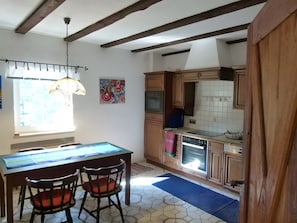 A kitchen with wooden cabinets, a dining table with chairs, a window with curtains, and a painting on the wall. - Apartment 'Hohlmühle Vogelsberg Hessen' with Absolute Seclusion, Wi-Fi, Private Terrace & Garden (Feldatal)