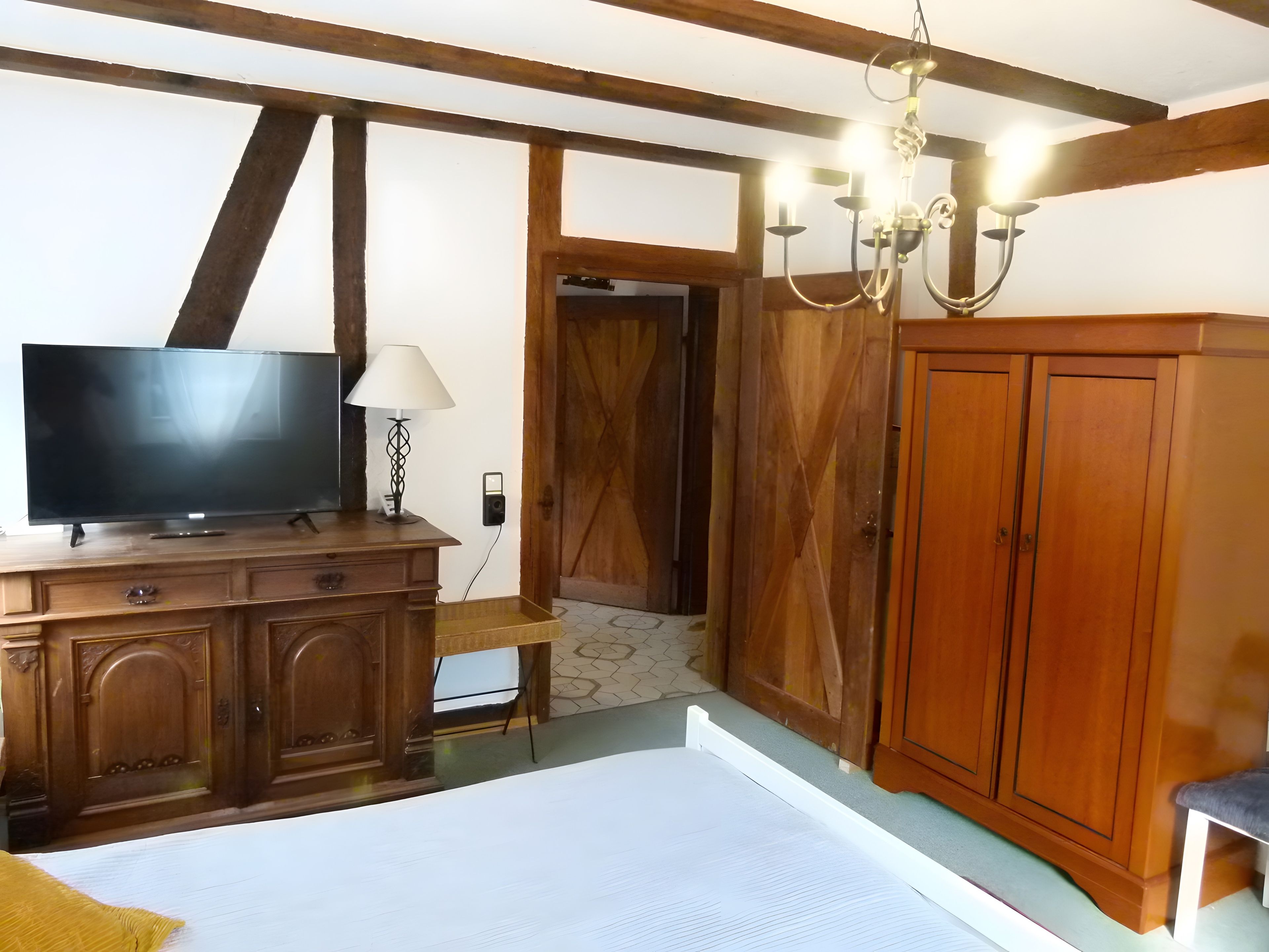 Een kamer met een televisie op een houten kast, een lamp, een kroonluchter en een garderobe.