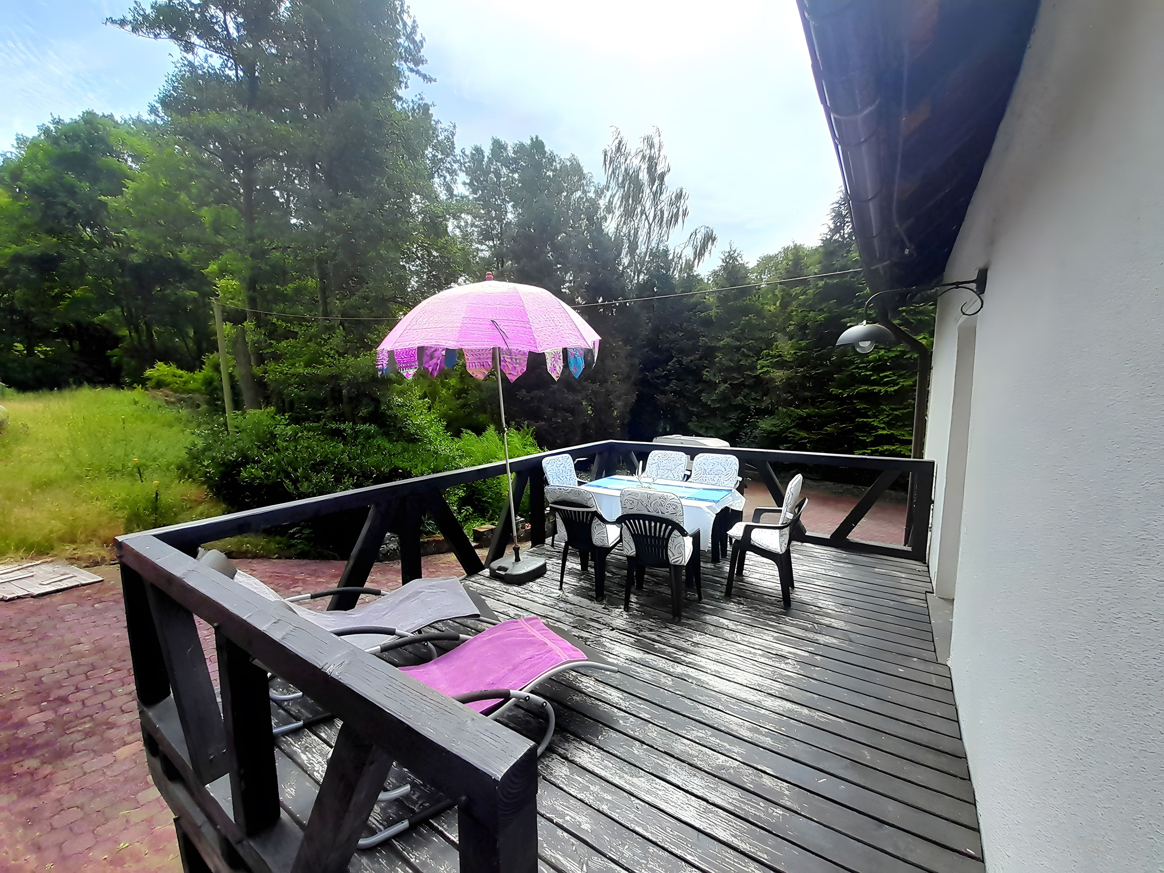 A wooden deck with a table and chairs, surrounded by greenery.