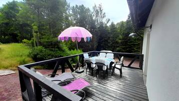 A wooden deck with a table and chairs, surrounded by greenery.