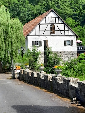 A traditional half-timbered house with a stone wall in front, surrounded by greenery. - Apartment 'Hohlmühle Vogelsberg Hessen' with Absolute Seclusion, Wi-Fi, Private Terrace & Garden (Feldatal)