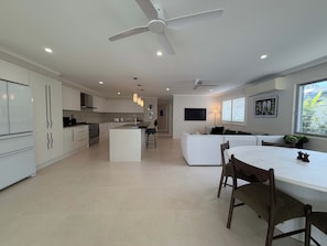 Una cucina moderna con isola centrale, un'area pranzo con tavolo e sedie bianche e una ventola a soffitto.