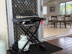 Ein tragbares Grill-Setup mit Propangasflasche, nahe einer Schiebetür, die zu einem Essbereich führt.