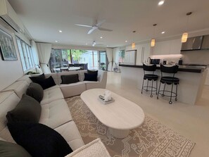 A modern living room with a sofa, a coffee table, and a kitchen area with a bar. - Maison du Lac - Boutique Coastal Escape (Currimundi)