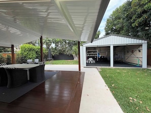 An outdoor patio area with a covered seating area, a barbecue grill, and a storage shed. - Maison du Lac - Boutique Coastal Escape (Currimundi)