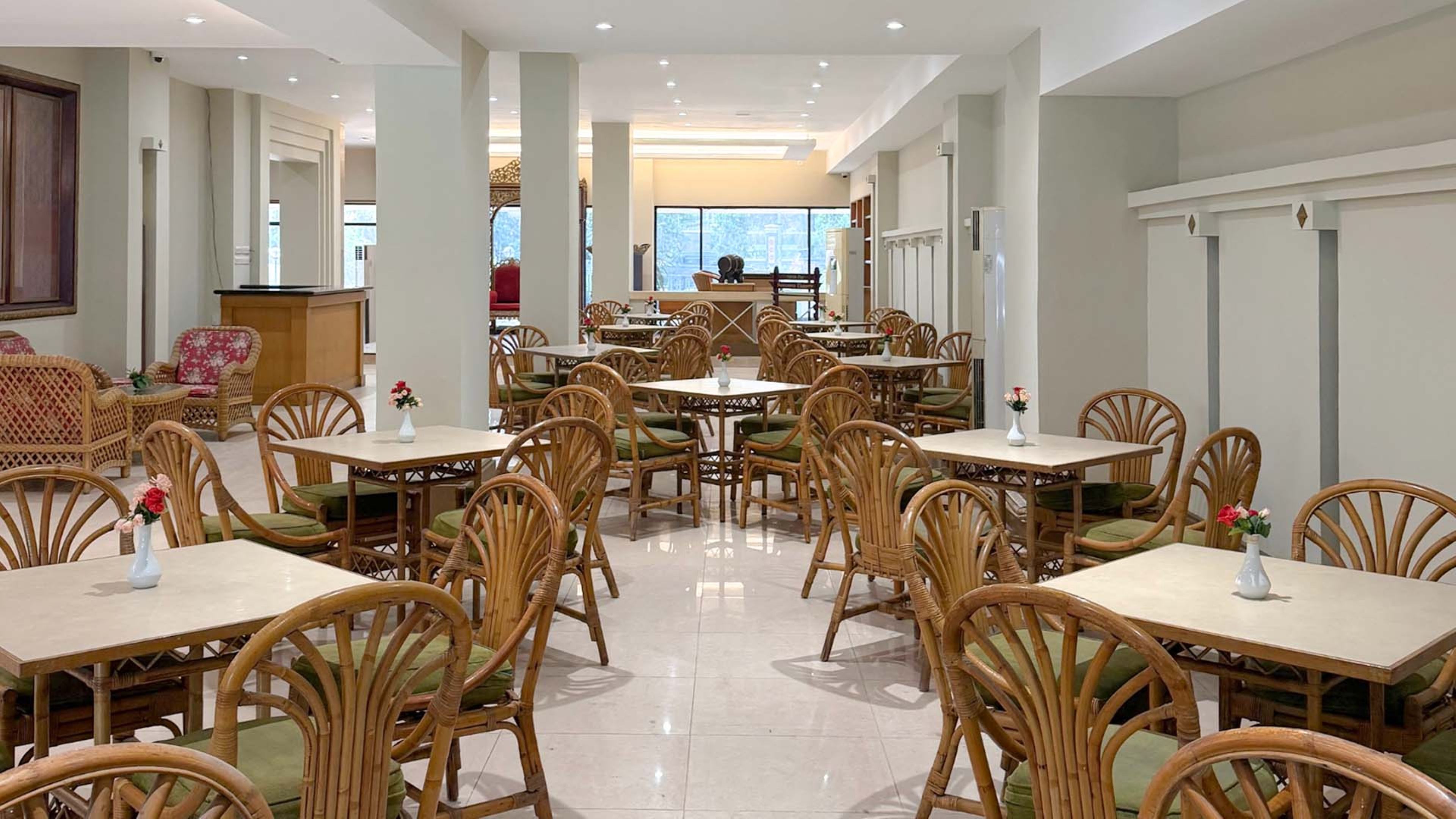 A hotel dining area with multiple tables and chairs, a reception desk, and a view of the outdoors.